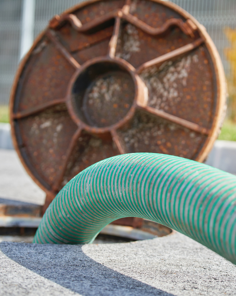 Green Suction Hose Entering an Open Manhole