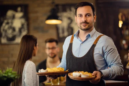 Man in a restaurant holding two plates of food with a blurred background
